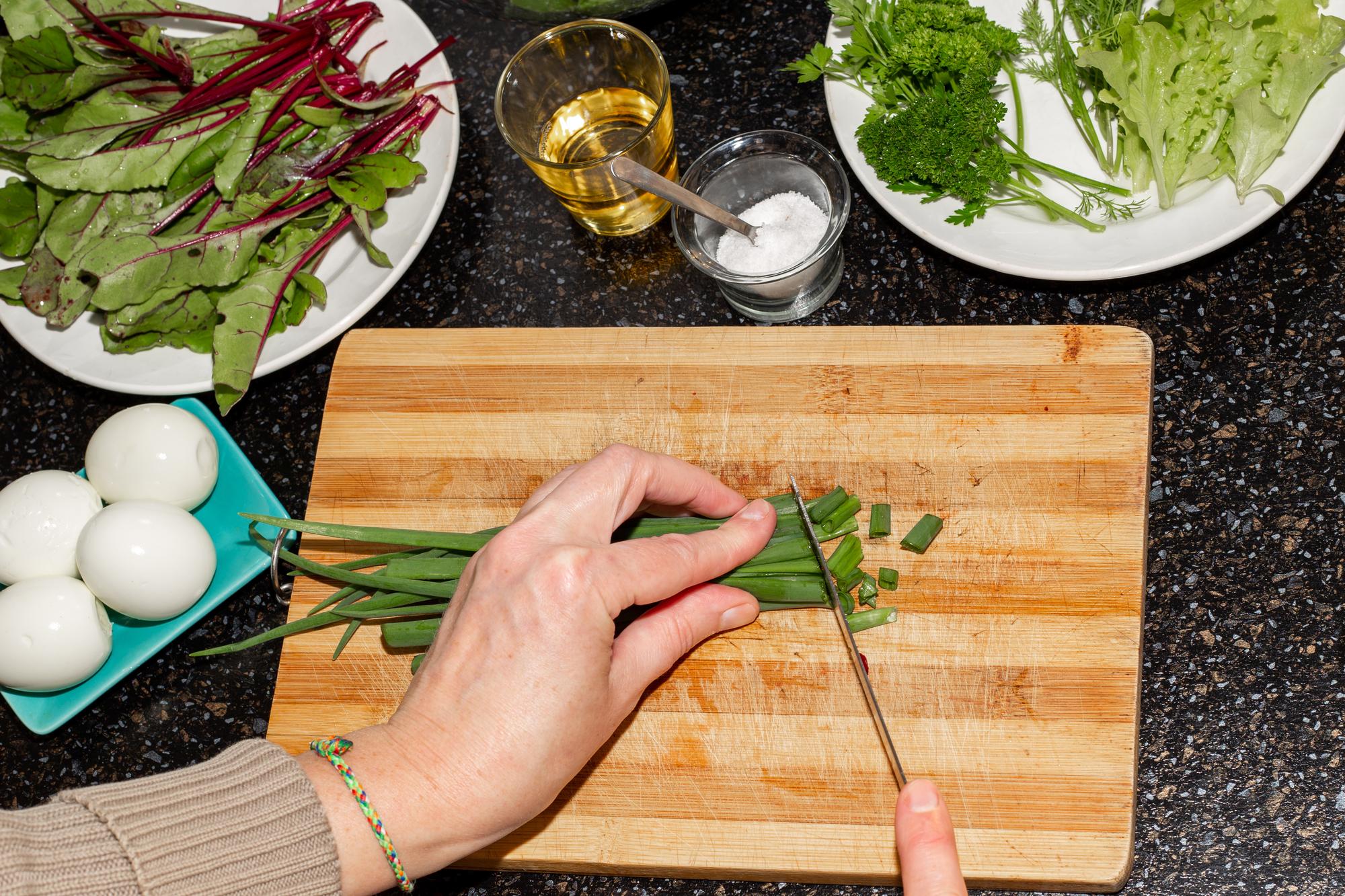 Hands slicing fresh herbs over cutting board